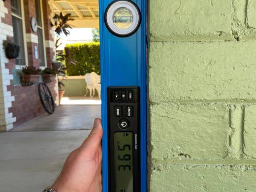 Digital level held against a masonry wall showing it is out of plumb