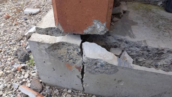 Cracked concrete footing exposed beside a brick wall