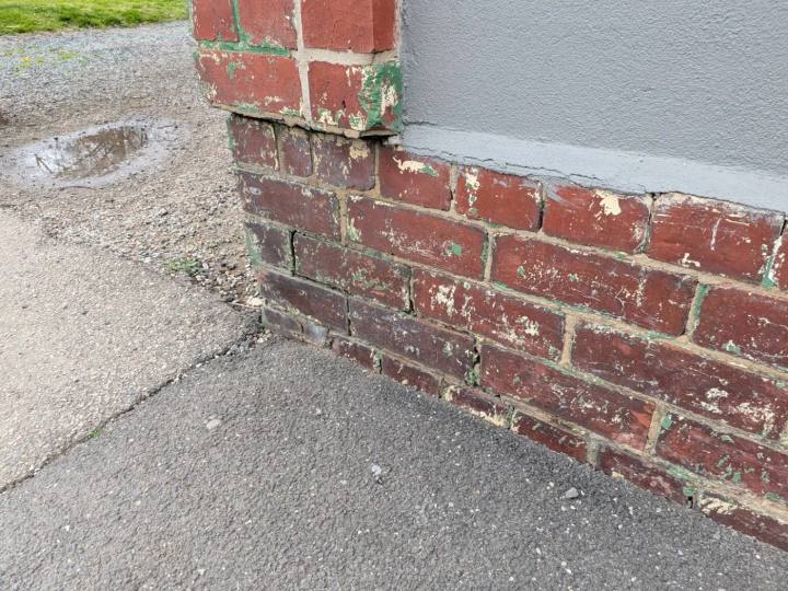 Cracked and displaced painted brickwork at the base of a wall